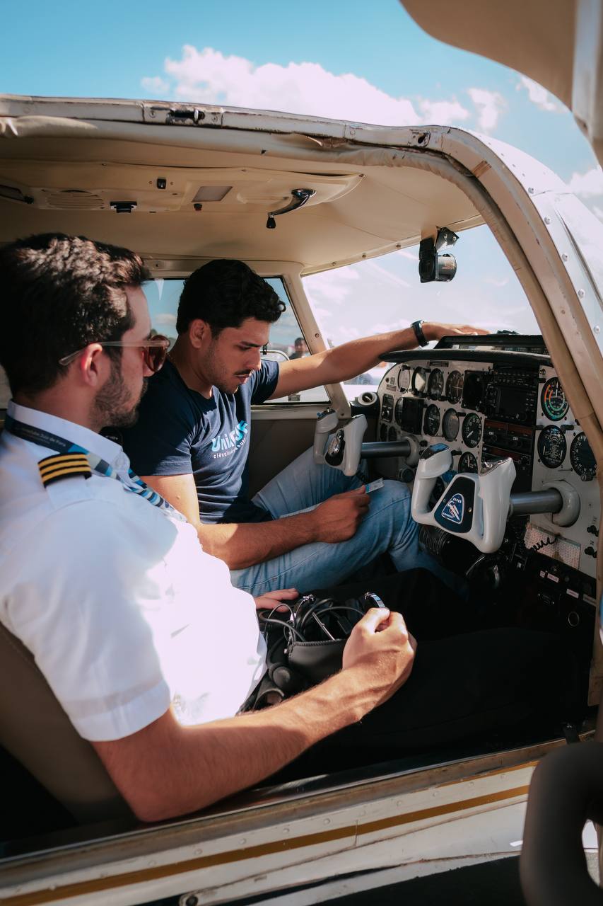 Instrutor de uniforme explicando o painel para o aluno dentro da aeronave