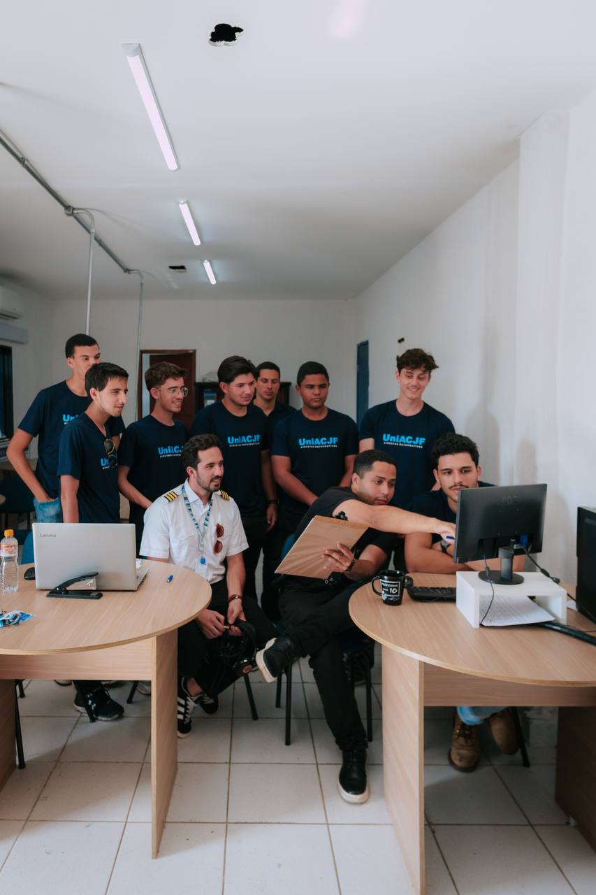 Turma de alunos e instrutor reunidos na sala, olhando o computador